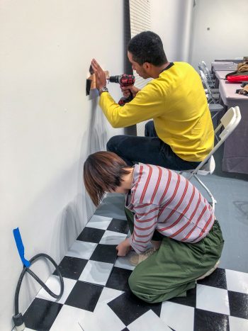 Yuchen Liu and Aren install faux tile and wall pegboard.
